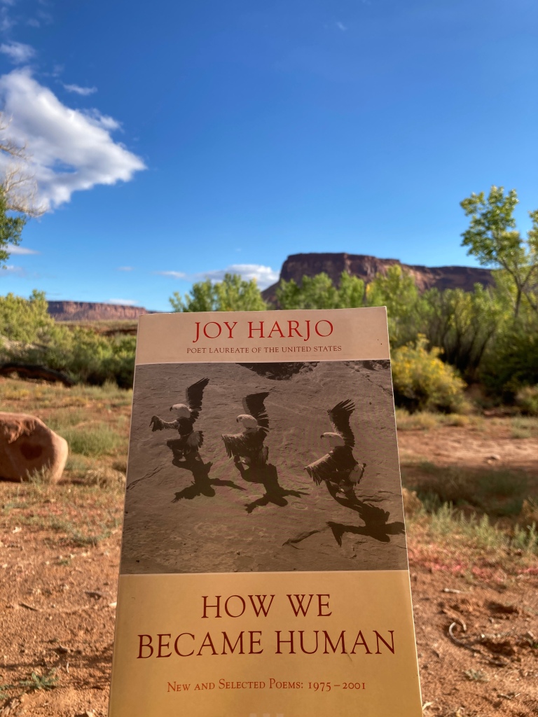 photo of Joy Harjo's How We Became Human with a red buttress, blue sky, and cottonwoods in the background